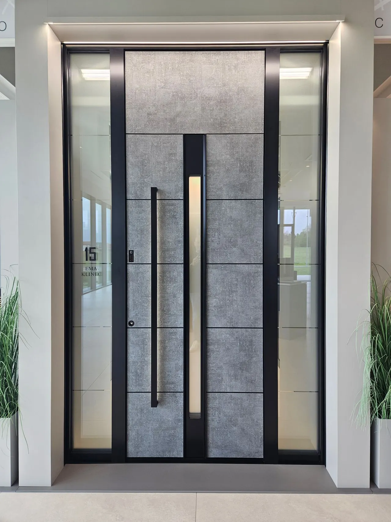 Porte d'entrée aluminium aspect béton avec vitrage vertical, longue barre de tirage noire et deux tierces vitrées