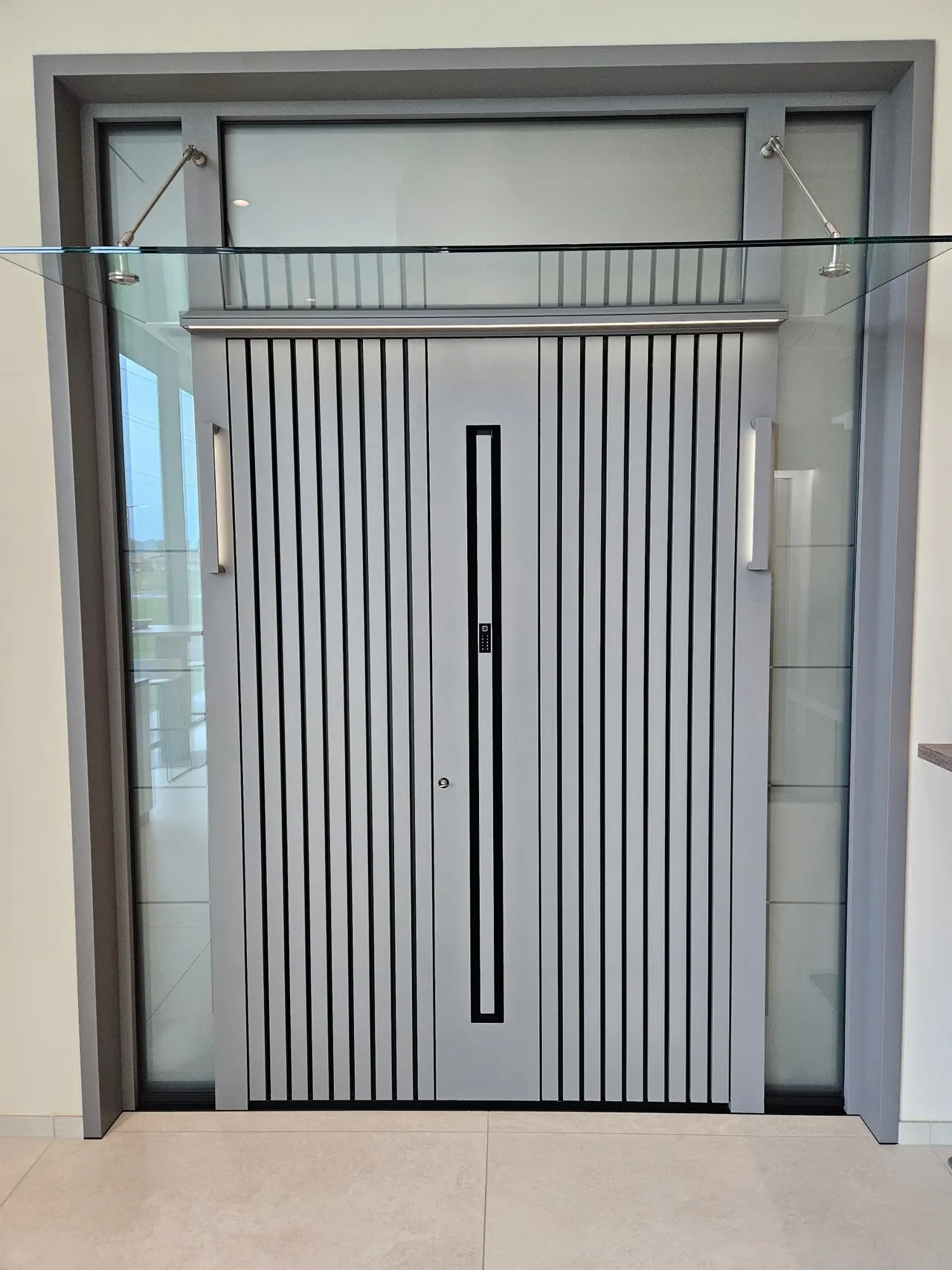 Porte d'entrée aluminium gris clair à lames verticales, imposte et tierces vitrées, auvent en verre