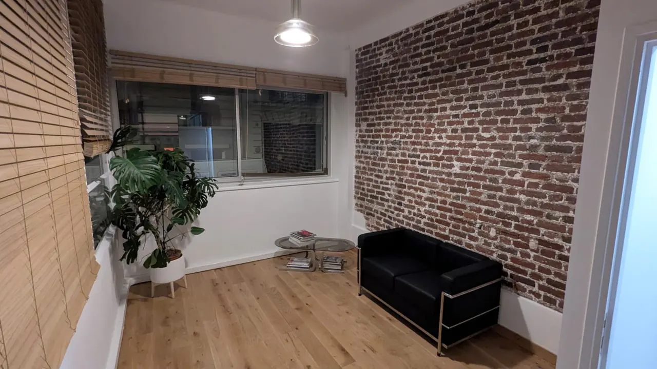 Petit salon avec mur de briques apparentes, parquet chêne et canapé noir