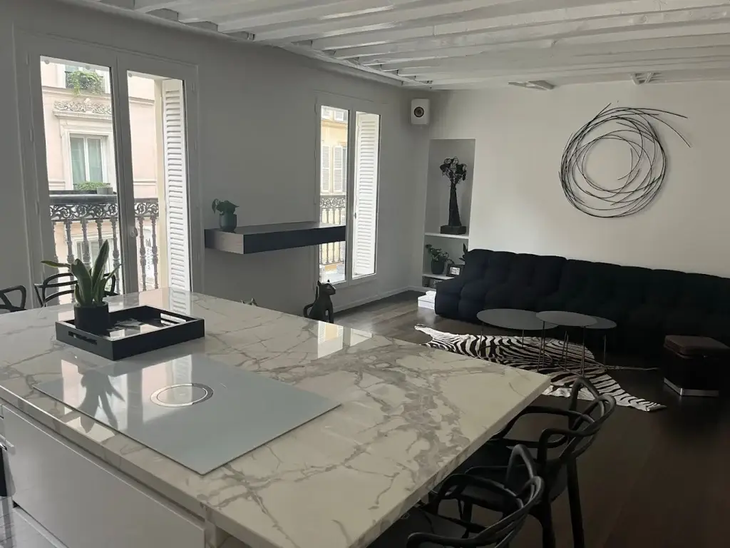 Îlot de cuisine en marbre blanc veiné avec plaque de cuisson intégrée, ouvert sur un séjour