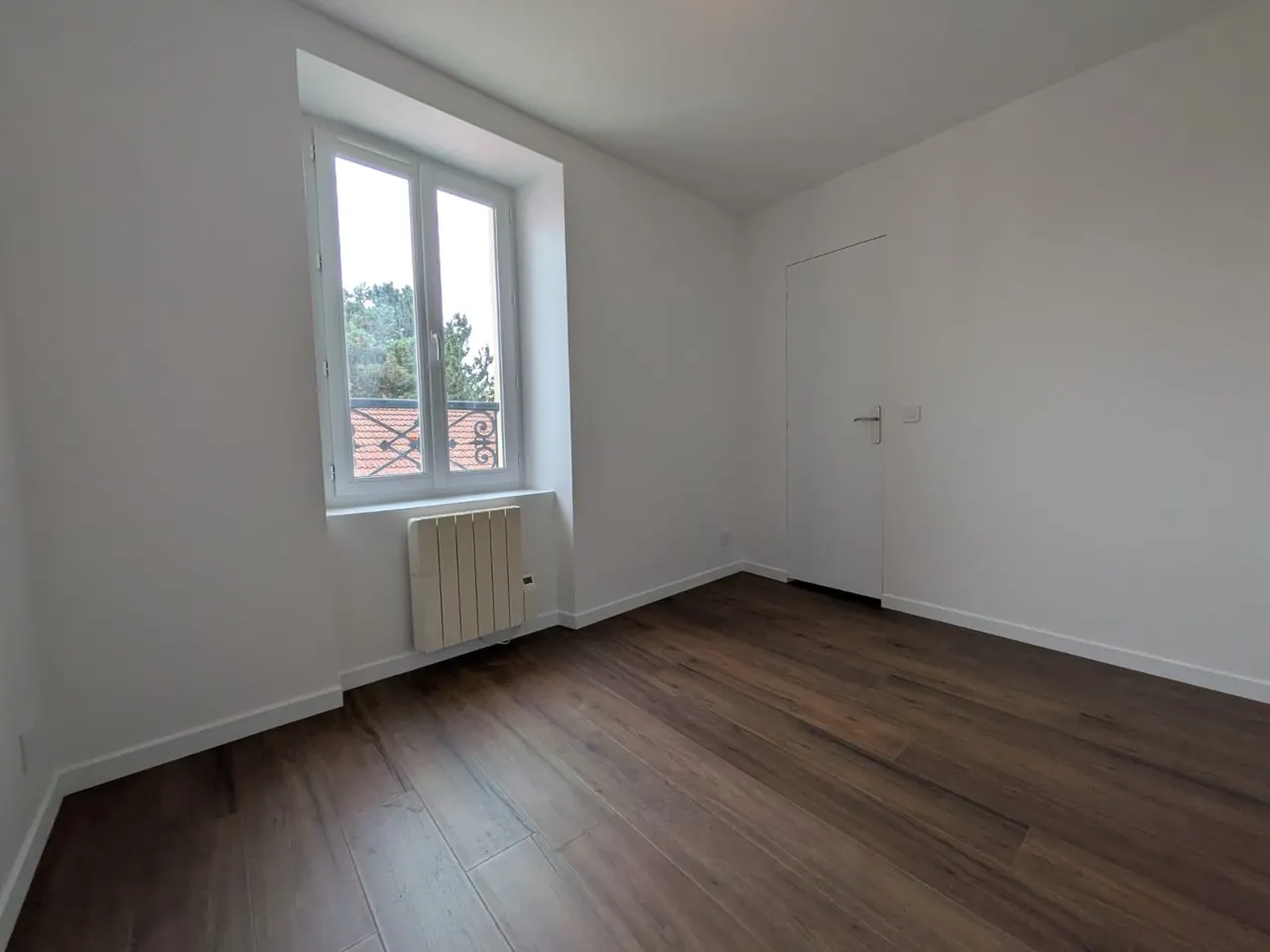 Chambre rénovée avec fenêtre, parquet foncé et porte blanche, à Meudon