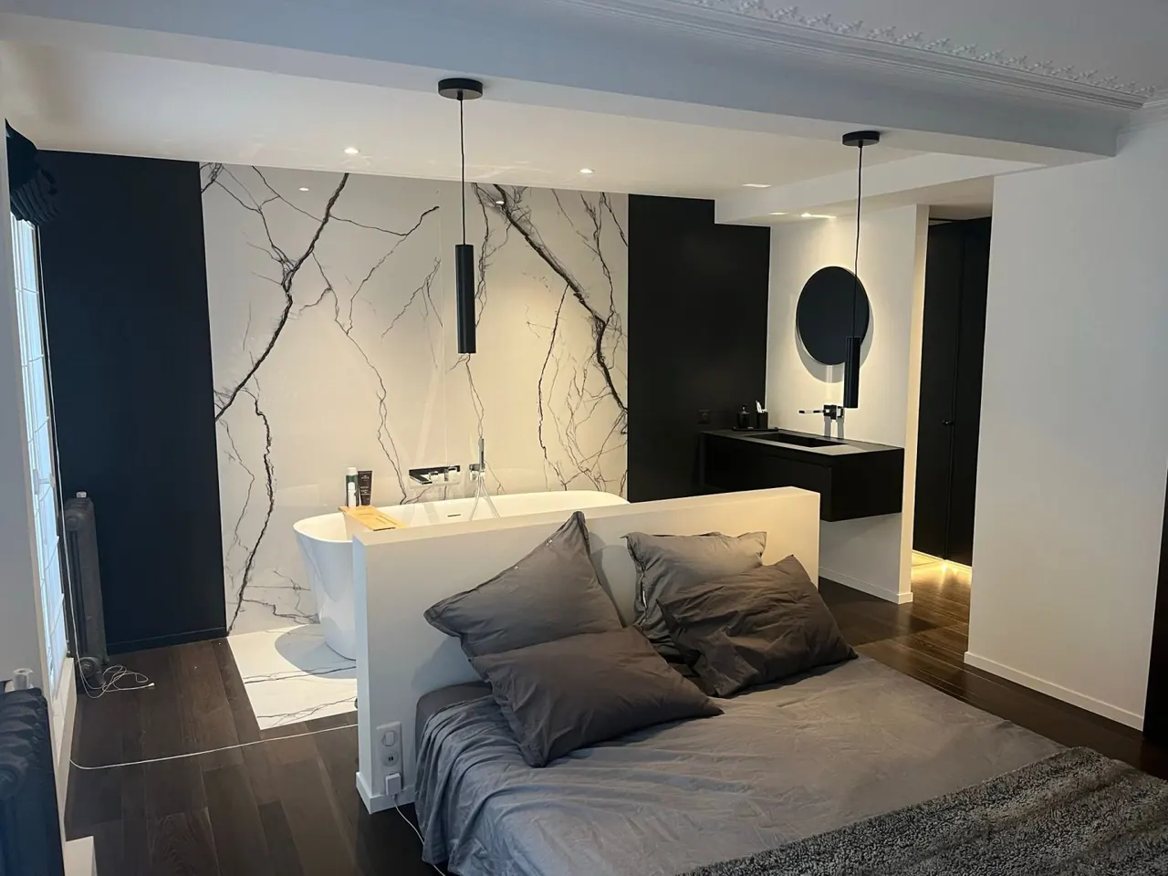 Chambre avec salle de bain ouverte, baignoire derrière une tête de lit, mur effet marbre