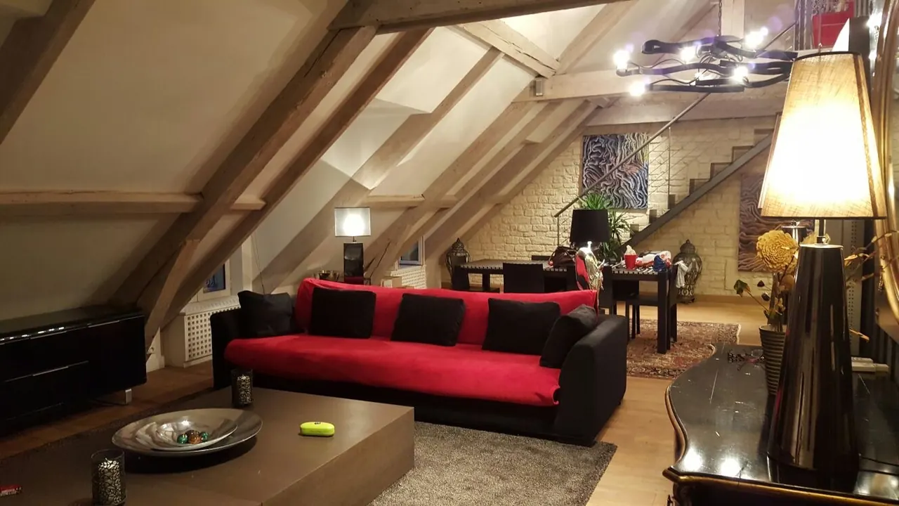 Séjour sous combles avec poutres apparentes, canapé rouge et mur de pierre peint